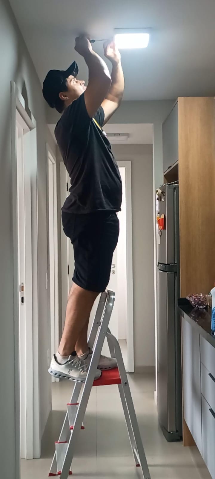 Profissional da JS Faz Tudo instalando uma luminária de teto no corredor de um apartamento